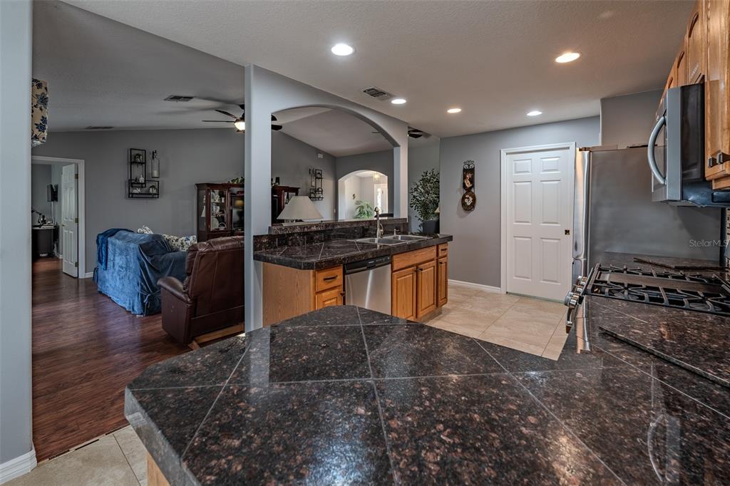 A kitchen with dark granite countertops and wood cabinets overlooks a living room area — 1708 SW 155TH PLACE ROAD, OCALA, FL