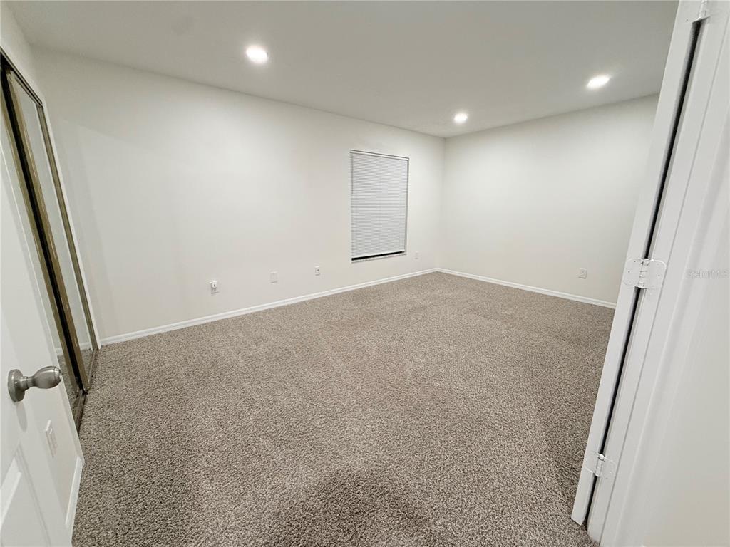 An empty bedroom features white walls, recessed lighting, beige carpeting, and a window with blinds — 6266 YORKTOWN DRIVE UNIT 179, ORLANDO, FL