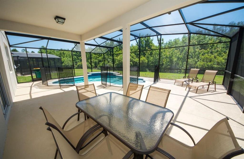 A covered patio features a glass dining table, lounge chairs, and a screened-in swimming pool — 4748 BLUE DIAMOND STREET, KISSIMMEE, FL