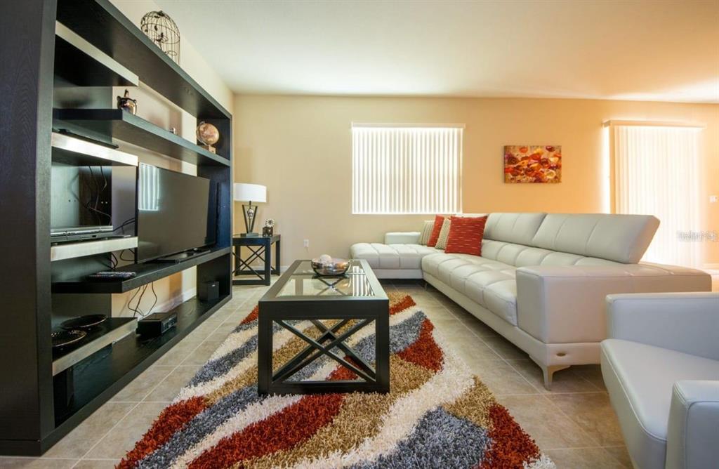 A living room features a white sectional sofa, a patterned rug, and a black shelving unit — 4748 BLUE DIAMOND STREET, KISSIMMEE, FL