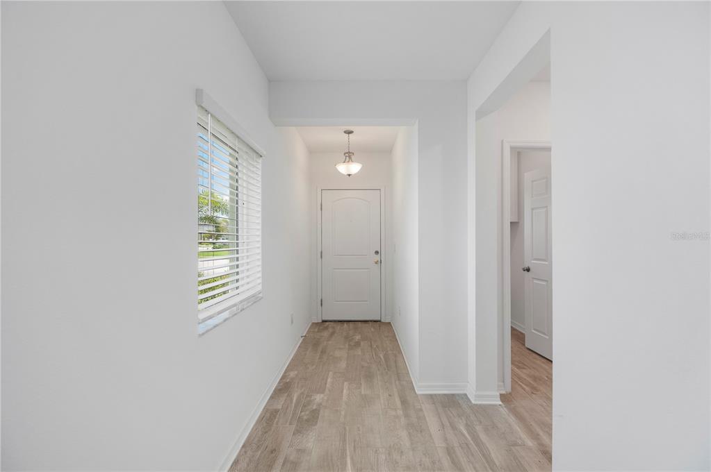 A bright entryway features white walls, light wood-look flooring, a window with blinds, and a door — 1968 SUNSET PRESERVE WAY, PORT CHARLOTTE, FL
