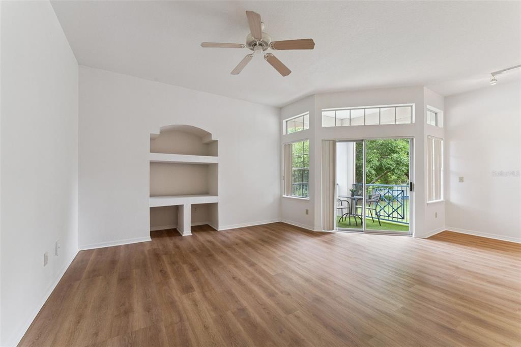 A living room with wood-look flooring, a built-in arched shelving unit, and a sliding glass door — 7270 WESTPOINTE BOULEVARD UNIT 931, ORLANDO, FL
