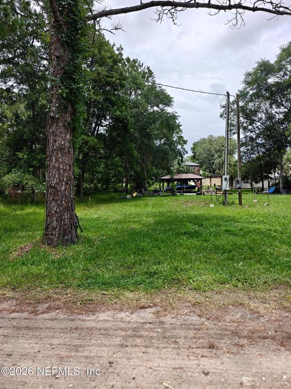 A grassy, wooded lot features a utility pole and a distant covered structure — 0 HIDE-A-WAY DRIVE, JACKSONVILLE, FL