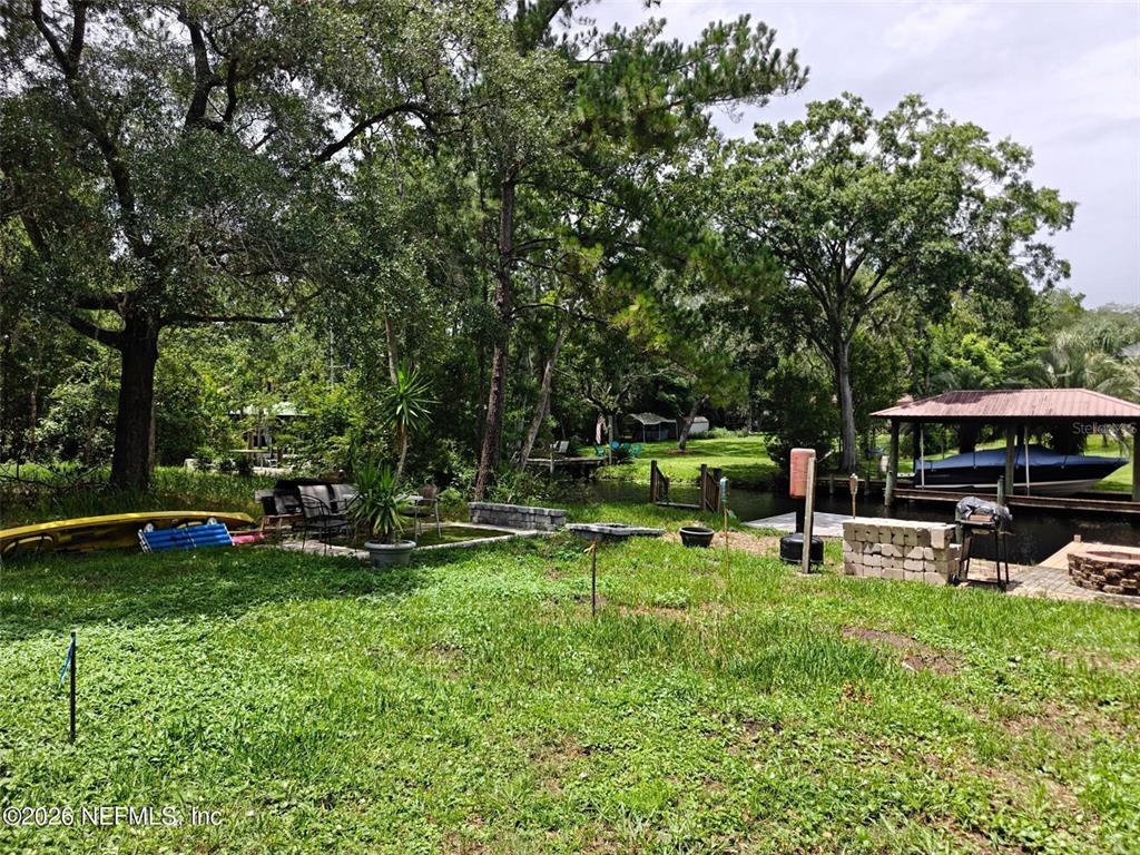 A grassy backyard features a boat dock, a covered boat slip, and mature trees — 0 HIDE-A-WAY DRIVE, JACKSONVILLE, FL