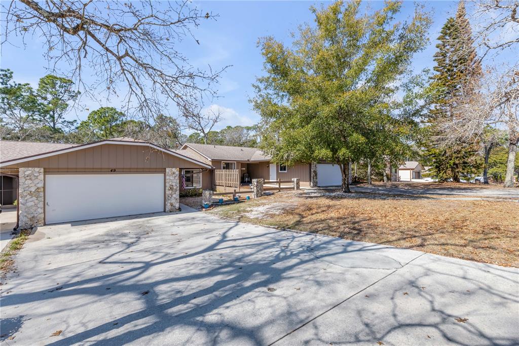 An aerial view of a single-story house with a shingled roof, garage, and wooded surroundings — 49 CROOKED PINE ROAD, PORT ORANGE, FL