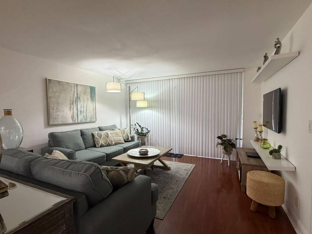 A living room features a gray sectional sofa, wood coffee table, and a wall-mounted television — 7011 Environ Boulevard # 210, Lauderhill FL 33319, LAUDERHILL, FL