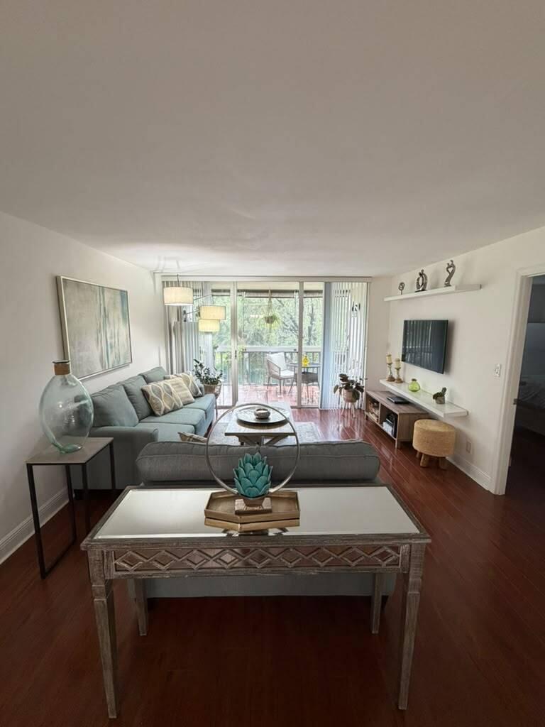 A living room features hardwood floors, a gray sofa, a mirrored console table, and a balcony — 7011 Environ Boulevard # 210, Lauderhill FL 33319, LAUDERHILL, FL
