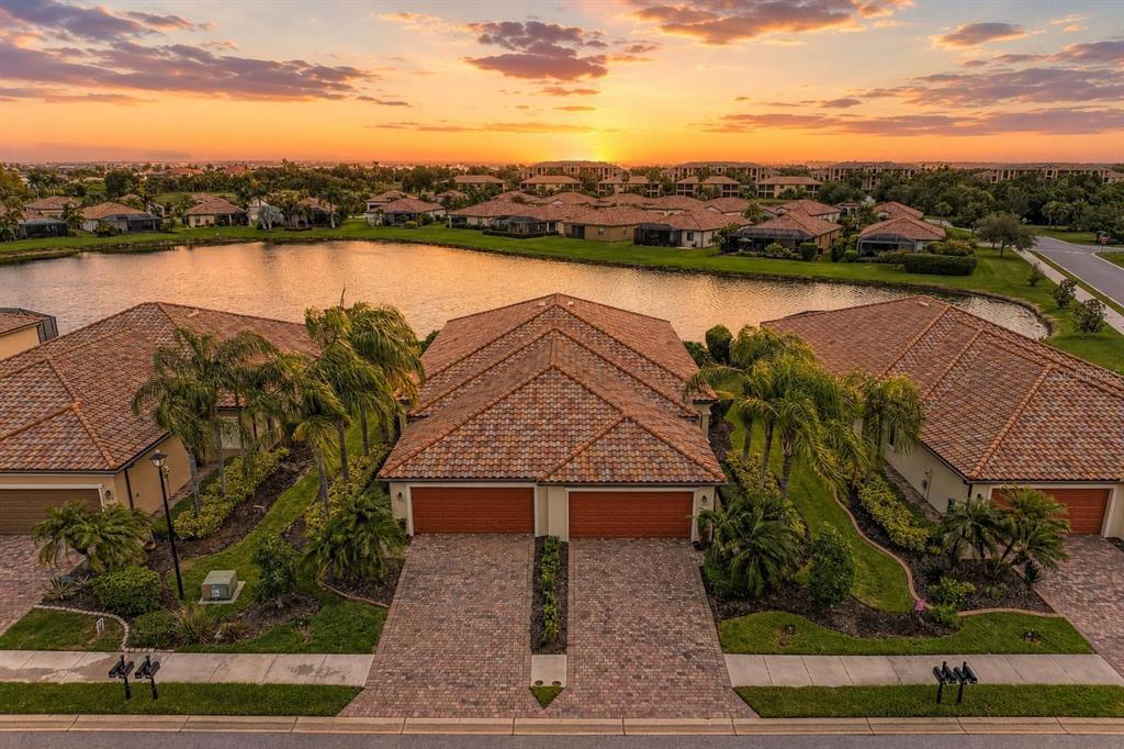 An aerial view of a suburban duplex with tiled roofs, brick driveways, and a lake — 6623 CANDLESTICK DRIVE, BRADENTON, FL