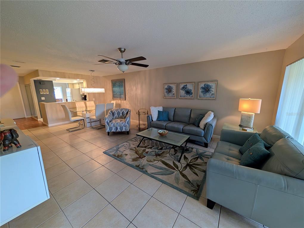 A living room with tile floors, a blue sofa set, and an adjacent dining area — 6896 W COUNTRY CLUB LANE UNIT 148, SARASOTA, FL