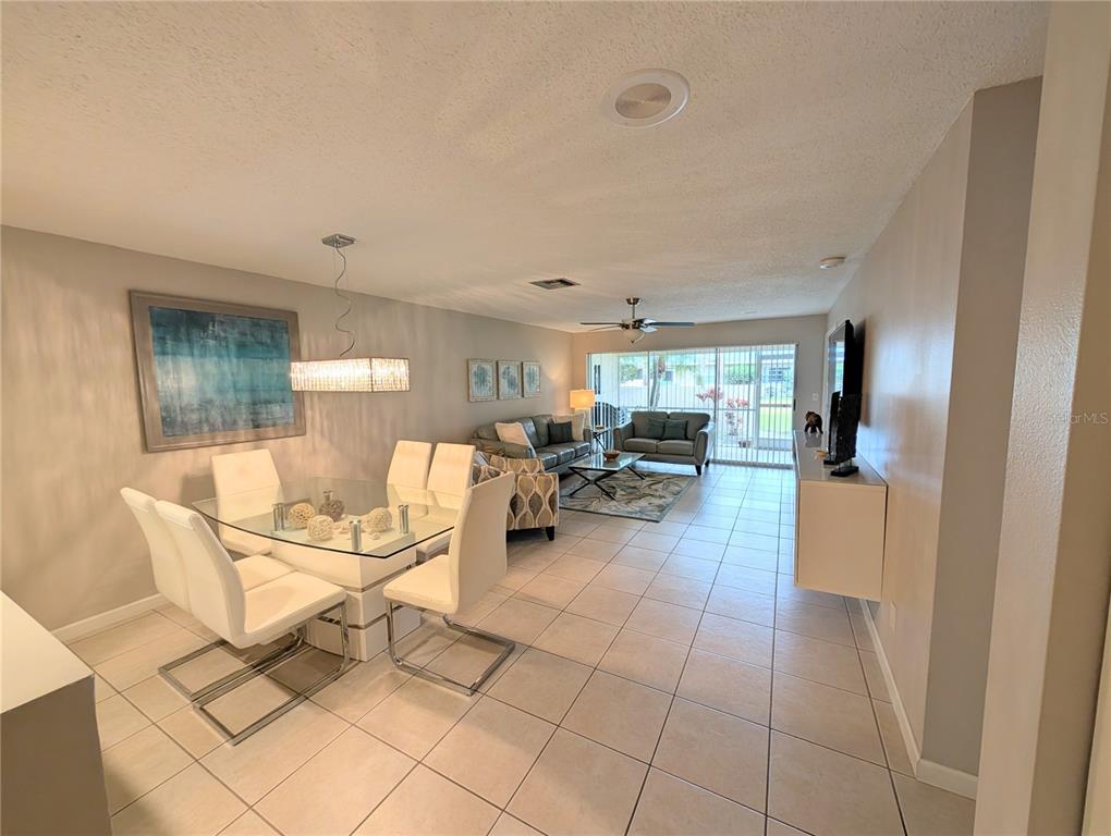 An open-concept living and dining area features tile flooring, white furniture, and sliding glass doors — 6896 W COUNTRY CLUB LANE UNIT 148, SARASOTA, FL