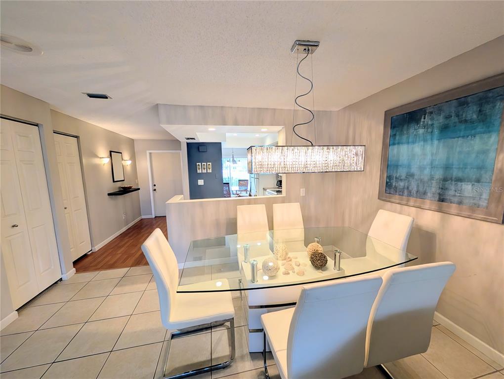 A dining room features a glass-top table, white chairs, and a modern rectangular pendant light — 6896 W COUNTRY CLUB LANE UNIT 148, SARASOTA, FL