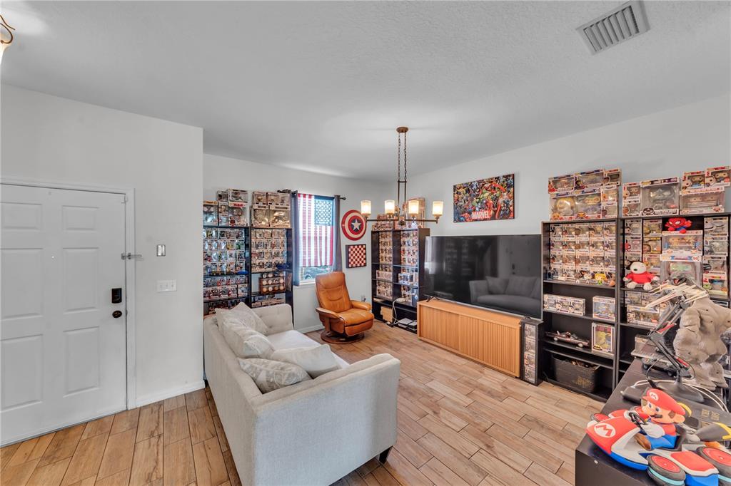 A living room features wood-look tile flooring, a sofa, a television, and numerous collectible figures — 1939 GREENWOOD VALLEY DRIVE, PLANT CITY, FL
