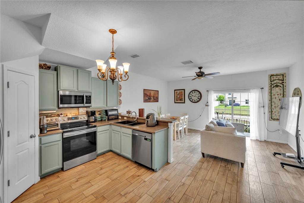 An open-concept kitchen with light green cabinets and stainless steel appliances overlooks a living area — 1939 GREENWOOD VALLEY DRIVE, PLANT CITY, FL