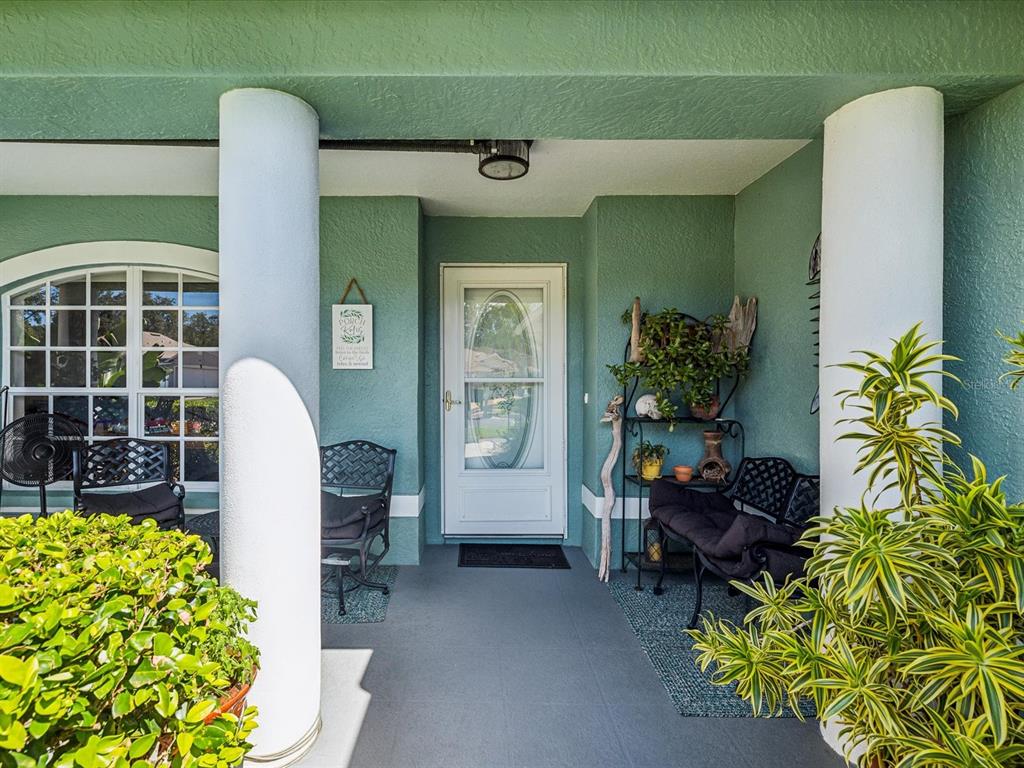 A covered front porch features green walls, white columns, and black metal patio furniture — 11404 TURTLE DOVE PLACE, NEW PORT RICHEY, FL