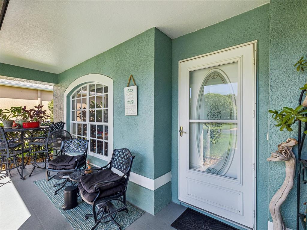 A covered front porch features teal stucco walls, a white storm door, and patio furniture — 11404 TURTLE DOVE PLACE, NEW PORT RICHEY, FL