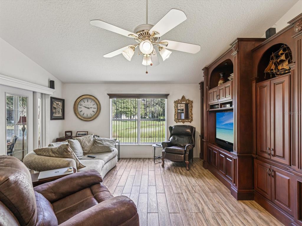 A living room features wood-look tile flooring, a ceiling fan, and a large wooden entertainment center — 11404 TURTLE DOVE PLACE, NEW PORT RICHEY, FL