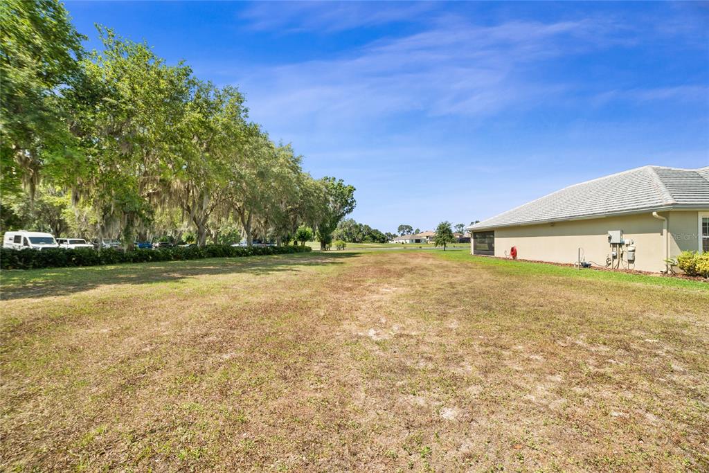 A grassy backyard lot sits adjacent to the side of a beige residential house — Lot F-20 EAGLES WAY WAY, TAVARES, FL
