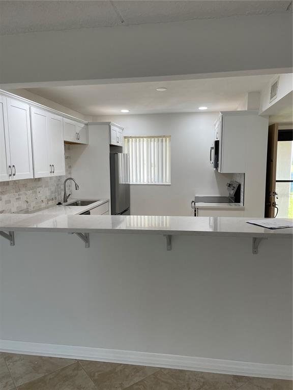 A kitchen features white cabinetry, a quartz breakfast bar, and stainless steel appliances — 845 S GULFVIEW BOULEVARD UNIT 110, CLEARWATER BEACH, FL