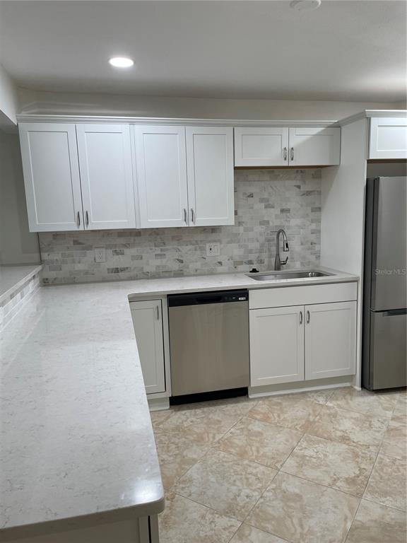 A kitchen features white cabinets, quartz countertops, a stainless steel dishwasher, and a tiled backsplash — 845 S GULFVIEW BOULEVARD UNIT 110, CLEARWATER BEACH, FL