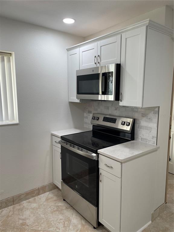 A kitchen features white cabinets, a stainless steel microwave, a black range, and tiled flooring — 845 S GULFVIEW BOULEVARD UNIT 110, CLEARWATER BEACH, FL