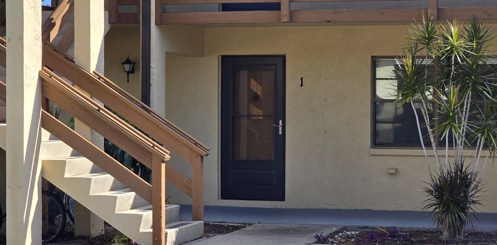 The exterior of a ground-floor apartment unit features a dark door, stairs, and a plant — 10 QUAILS RUN BOULEVARD UNIT 1, ENGLEWOOD, FL