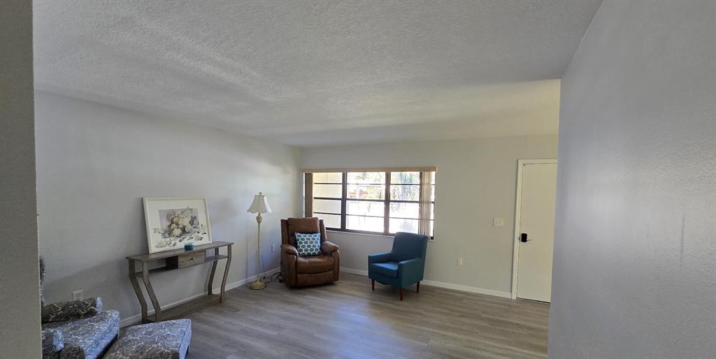 A living room features light gray walls, wood-look flooring, a window, and several chairs — 10 QUAILS RUN BOULEVARD UNIT 1, ENGLEWOOD, FL