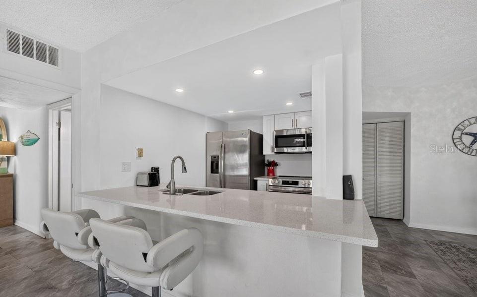 A kitchen with white cabinets, stainless steel appliances, and a breakfast bar with two stools — 3600 S OCEAN SHORE BOULEVARD UNIT 111, FLAGLER BEACH, FL
