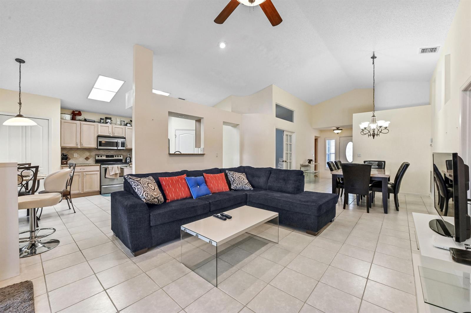 An open-concept living room features a dark sectional sofa, tile flooring, and a kitchen area — 2241 Soundings Court, FL 33413, FL