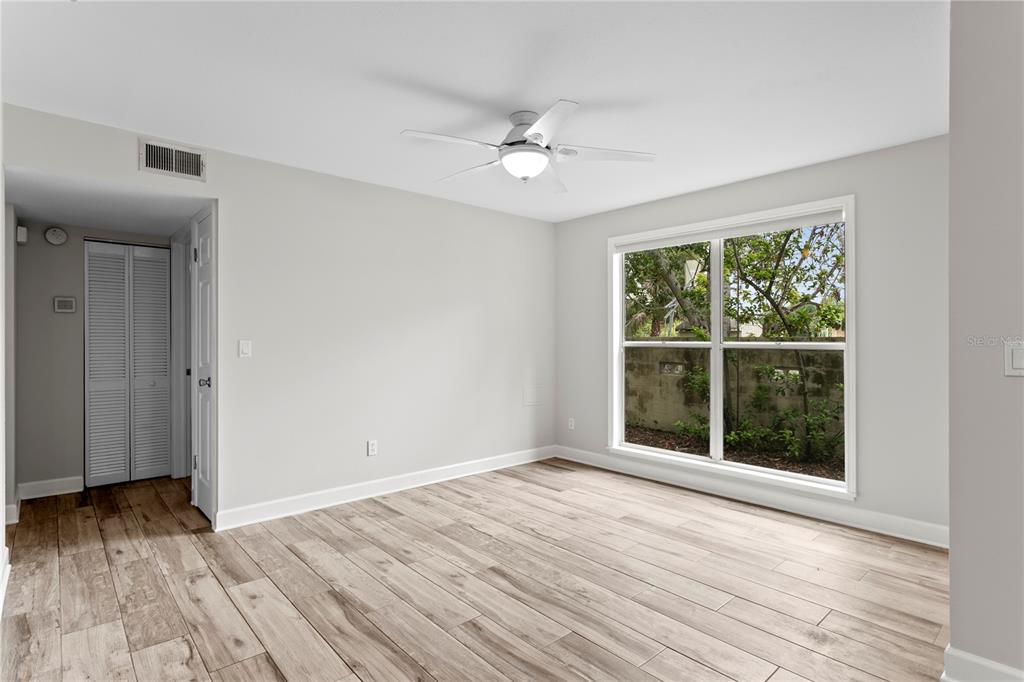 An empty bedroom features light wood-look flooring, a ceiling fan, and a large window — 606 S ALBANY AVENUE UNIT 17, TAMPA, FL