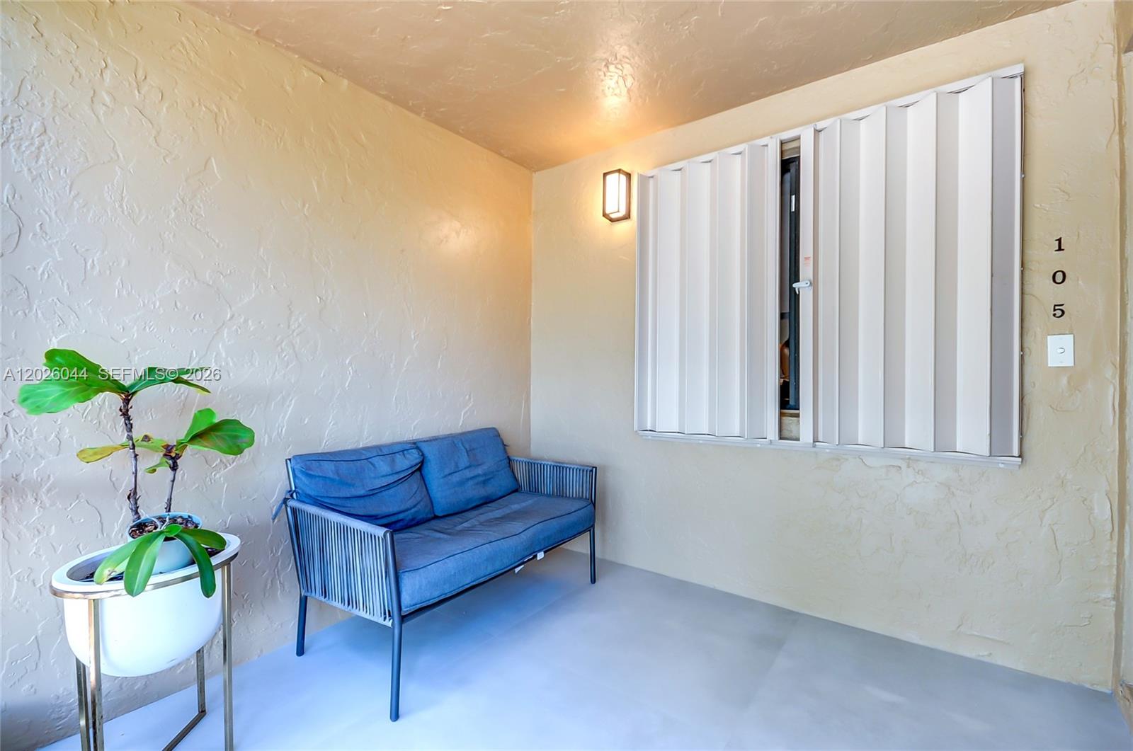 A small covered patio features a blue loveseat, a potted plant, and accordion storm shutters — 302 Lakeview Dr # 105, Weston FL 33326, WESTON, FL