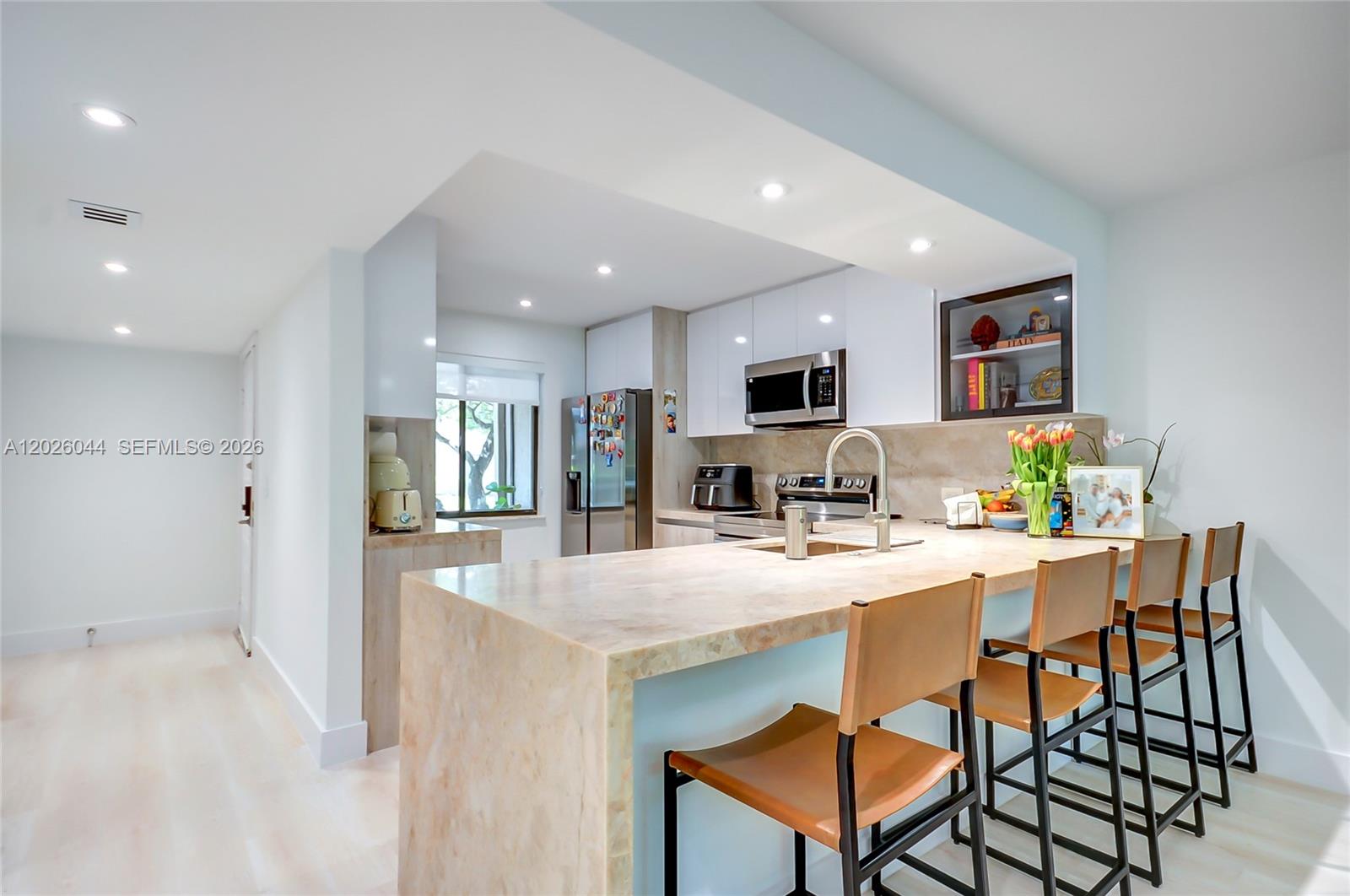 A modern kitchen features a stone waterfall island, white cabinetry, and four leather bar stools — 302 Lakeview Dr # 105, Weston FL 33326, WESTON, FL