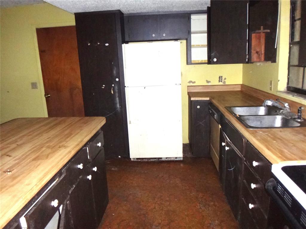 A kitchen features dark cabinets, wood countertops, a white refrigerator, and yellow walls — 7556 23RD STREET, ZEPHYRHILLS, FL