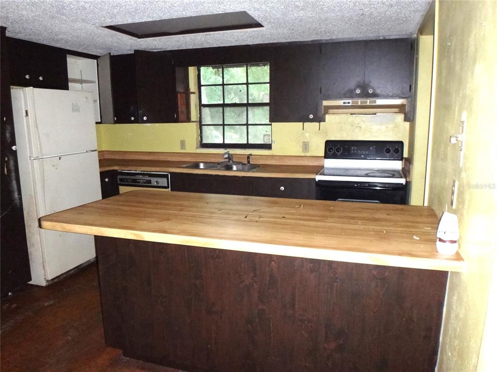 A kitchen features dark wood cabinets, a butcher block island, and a white refrigerator — 7556 23RD STREET, ZEPHYRHILLS, FL