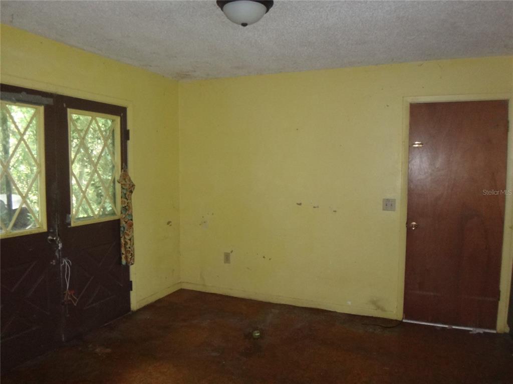 An interior room with yellow walls, a brown door, a glass-paneled door, and concrete flooring — 7556 23RD STREET, ZEPHYRHILLS, FL