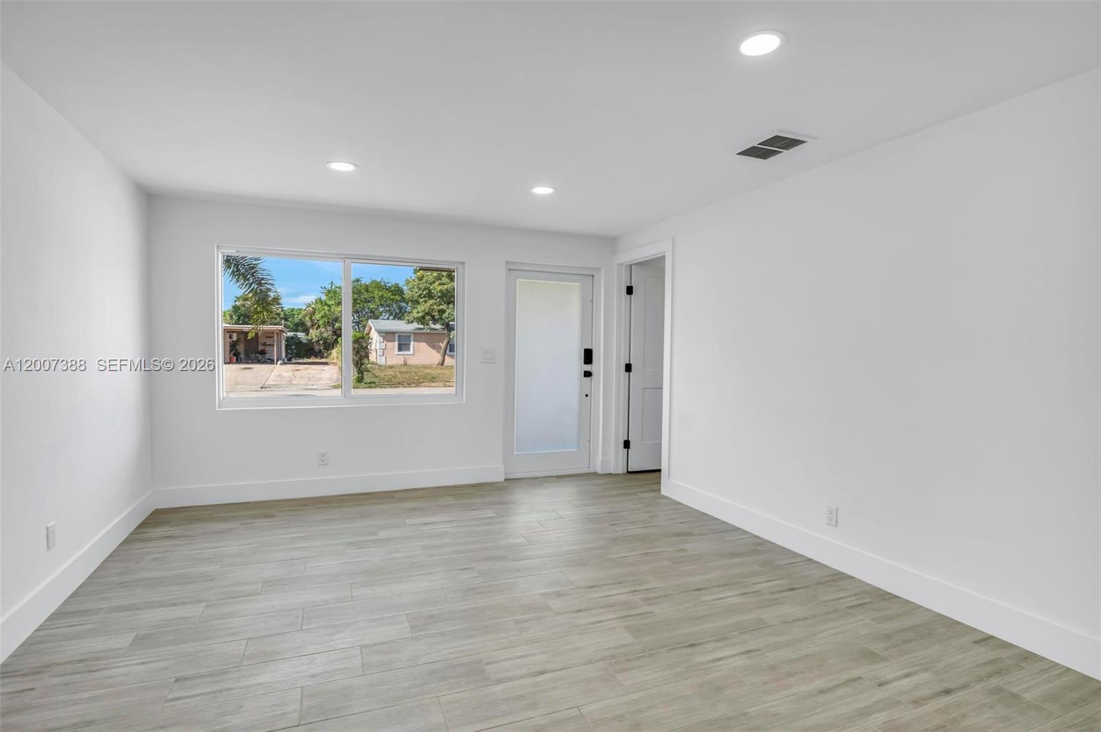A bright, empty room features white walls, light wood-look tile flooring, and a glass-paneled door — 311 NW 12th Ave, Delray Beach FL 33444, DELRAY BEACH, FL