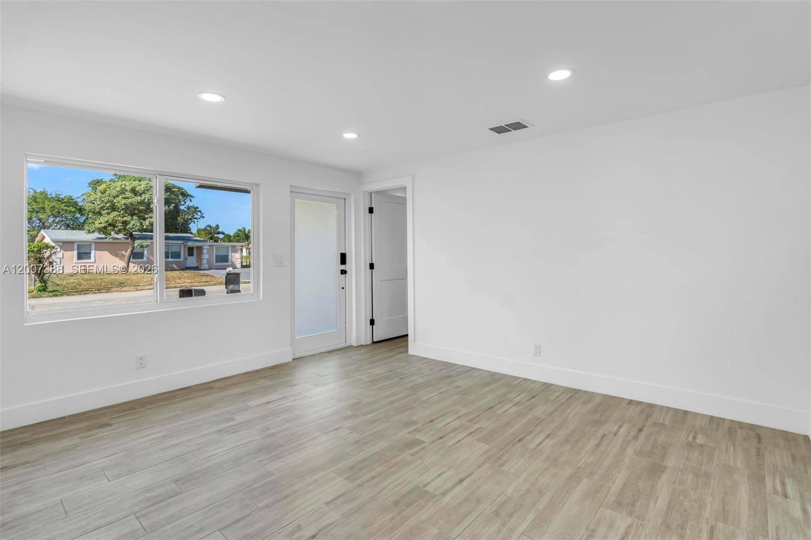 A bright, empty room features white walls, light wood-look flooring, and a large window — 311 NW 12th Ave, Delray Beach FL 33444, DELRAY BEACH, FL