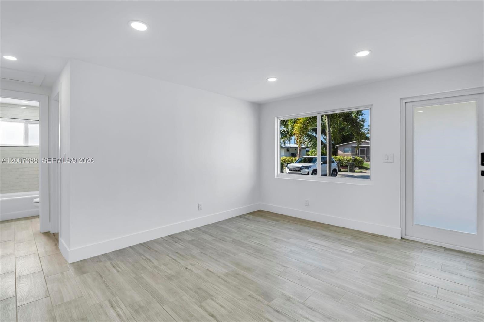 A bright, empty room features white walls, light wood-look flooring, a window, and a door — 311 NW 12th Ave, Delray Beach FL 33444, DELRAY BEACH, FL