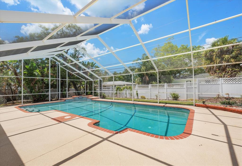 A rectangular swimming pool with a spa is enclosed by a white screen lanai — 802 ALLAMANDA DRIVE, LARGO, FL