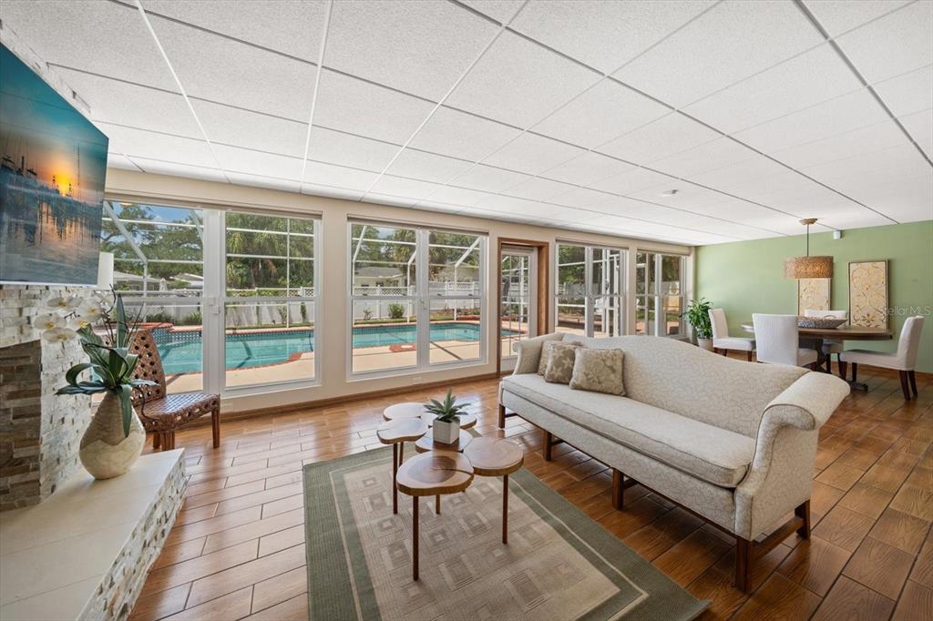 A living room with a stone fireplace, wood-look tile floors, and views of a pool — 802 ALLAMANDA DRIVE, LARGO, FL