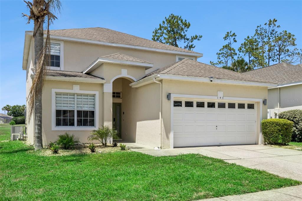 A two-story, beige stucco house with a two-car garage and a front lawn — 147 TROON CIRCLE, DAVENPORT, FL