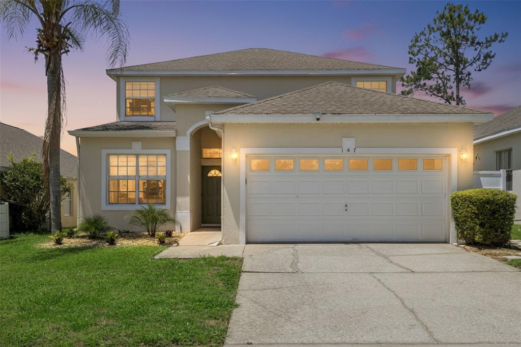 A two-story suburban house with a beige stucco exterior, a two-car garage, and a palm tree — 147 TROON CIRCLE, DAVENPORT, FL