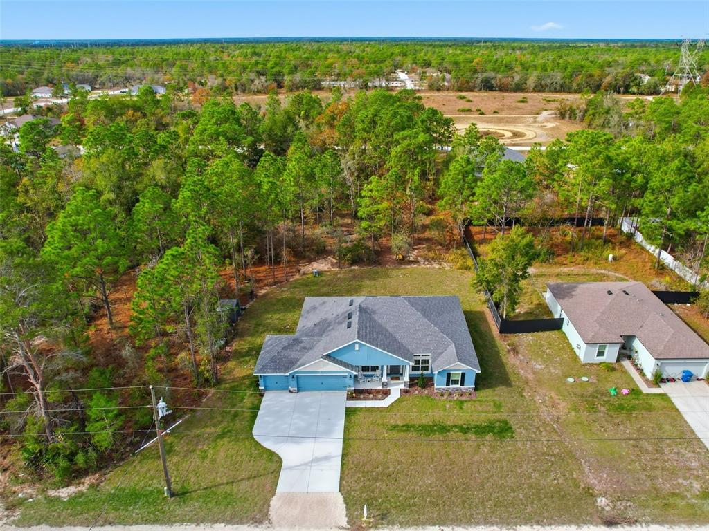 An aerial view shows a blue house with a gray roof surrounded by wooded land — 14351 CAROLINA CHICKADEE ROAD, WEEKI WACHEE, FL