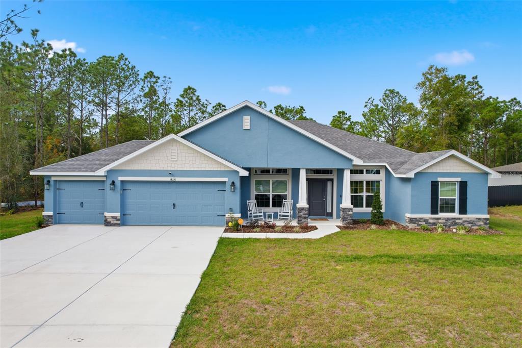 A blue single-story house with a three-car garage, stone accents, and a concrete driveway — 14351 CAROLINA CHICKADEE ROAD, WEEKI WACHEE, FL