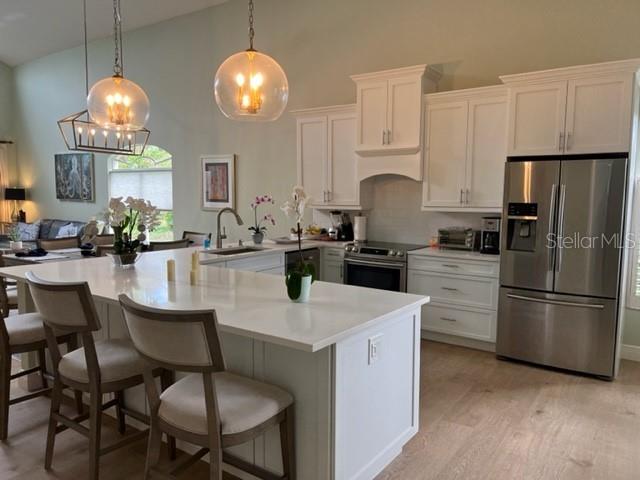 A modern kitchen features white cabinetry, a large island with bar seating, and stainless appliances — 8784 PEBBLE CREEK LANE, SARASOTA, FL