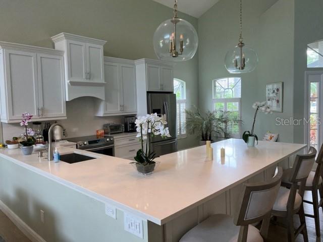 A kitchen features white cabinetry, a large quartz island, and two glass globe pendant lights — 8784 PEBBLE CREEK LANE, SARASOTA, FL