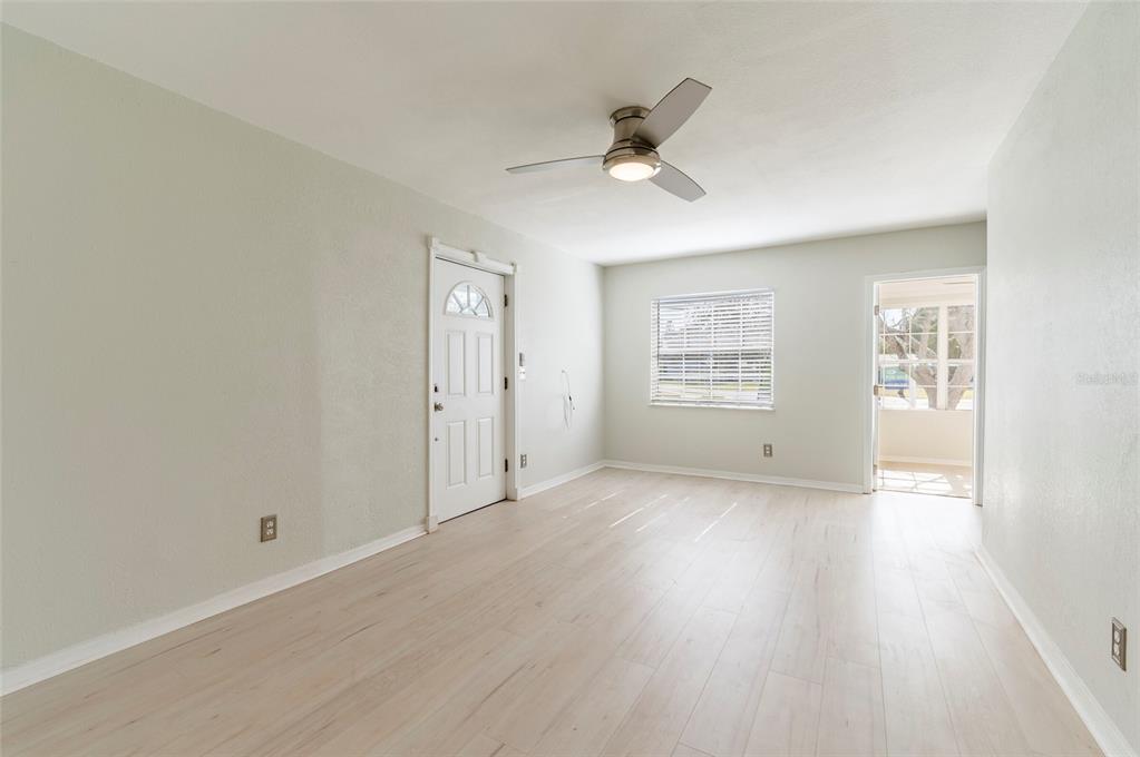 An empty room features light-colored wood-look flooring, a ceiling fan, a white door, and a window — 6699 78TH AVENUE N, PINELLAS PARK, FL