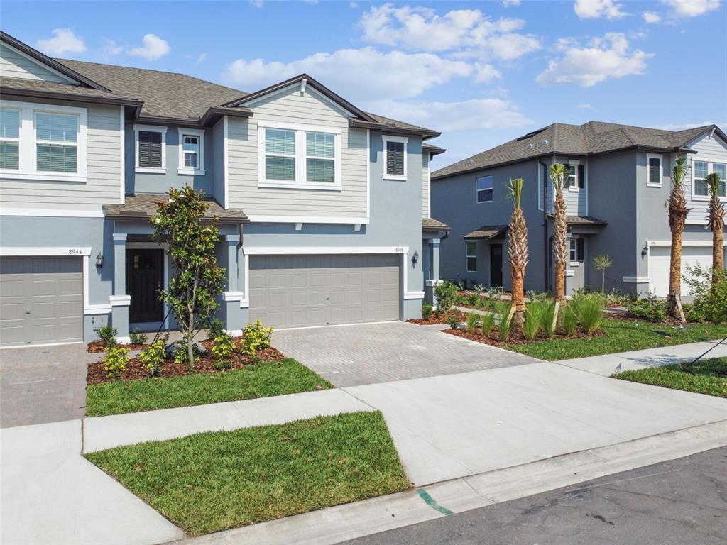 Two-story townhouses with gray siding, attached garages, and small front yards under a blue sky — 8938 GALLANTREE PLACE, LAND O LAKES, FL