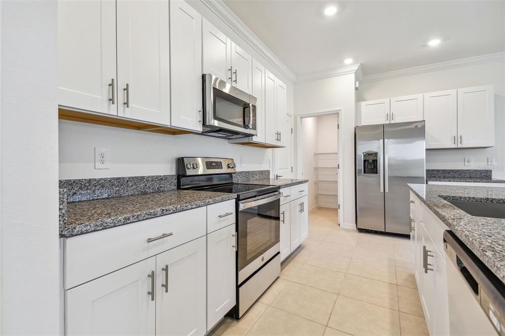 A kitchen features white cabinets, granite countertops, stainless steel appliances, and a walk-in pantry — 8938 GALLANTREE PLACE, LAND O LAKES, FL