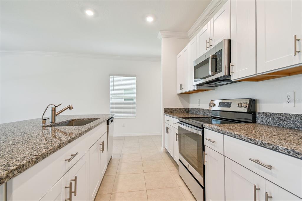 A kitchen features white cabinets, granite countertops, stainless steel appliances, and tile flooring — 8938 GALLANTREE PLACE, LAND O LAKES, FL