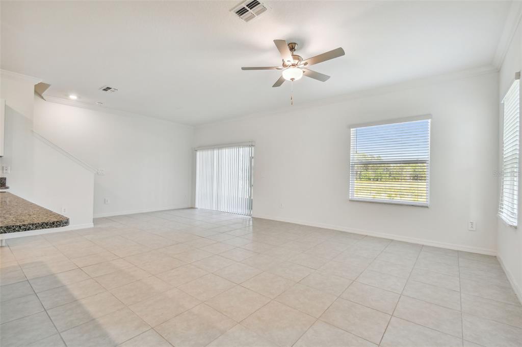 A bright, open-concept living room features white walls, tile flooring, and a ceiling fan — 8938 GALLANTREE PLACE, LAND O LAKES, FL